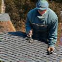 A roofer carefully nailing down a shingle on a roof.